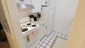 A compact kitchen with white cabinets, a stove, a refrigerator, and a tiled floor. - Capitol Hill & Penn - Steps from Eastern Market (Washington)