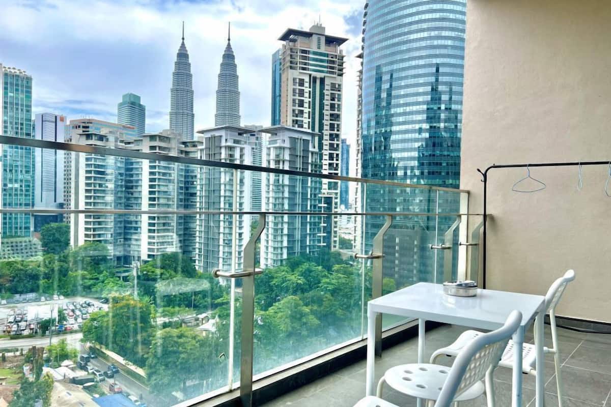 Ein Balkon mit Glastrennwand, einem weißen Tisch und zwei weißen Stühlen. Im Hintergrund Hochhäuser und ein Blick auf die Stadt.