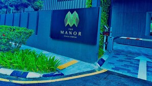 A sign for "The Manor Kuala Lumpur" with a modern building in the background.