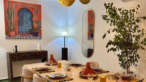 A dining area with a long table set for a meal, surrounded by chairs, a hanging light fixture, and decorative elements including a mirror and artwork. - Magnificent Riad Kechmya 5 suites bassin Rooftop Proche Jemaa El Fna Majorelle  (Marrakesh)