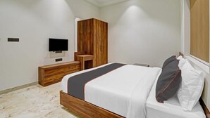 A modern bedroom with a wooden bed frame, a flat-screen TV mounted on the wall, and a wooden wardrobe. - HOTEL RATNA VILAS PALACE (Rajkot)