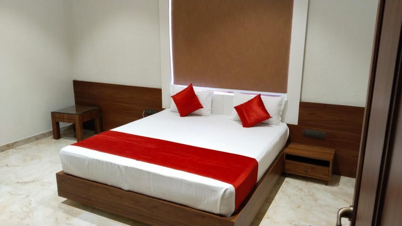 A neatly made bed with a red accent, a wooden headboard, a bedside table, and a nightstand.