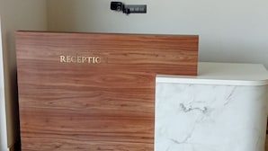 A reception area with a wooden reception desk labeled "RECEPTION" and a white marble counter. - HOTEL RATNA VILAS PALACE (Rajkot)