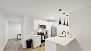 A modern kitchen with white cabinetry, a stainless steel refrigerator, a microwave, and a sink with a black faucet.