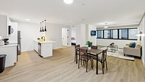 A modern kitchen with white cabinets, a dining area with a wooden table and chairs, and a large window providing natural light.