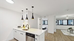 A modern kitchen with white cabinetry, a dishwasher, and pendant lighting.