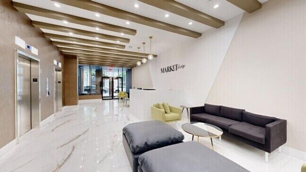 A modern lobby with a marble floor, a dark sofa, a yellow armchair, and a white reception desk.