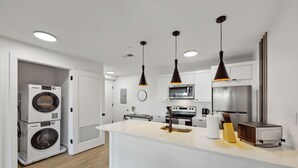 A modern kitchen with a central island, built-in appliances, pendant lighting, and a visible laundry area.