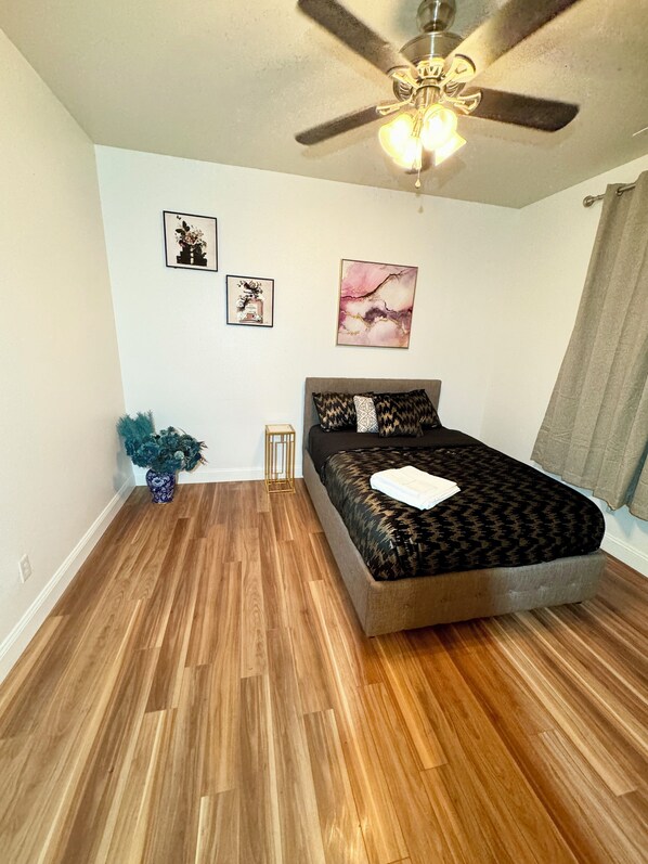 A bedroom with a bed, a ceiling fan, and three framed pictures on the wall.
