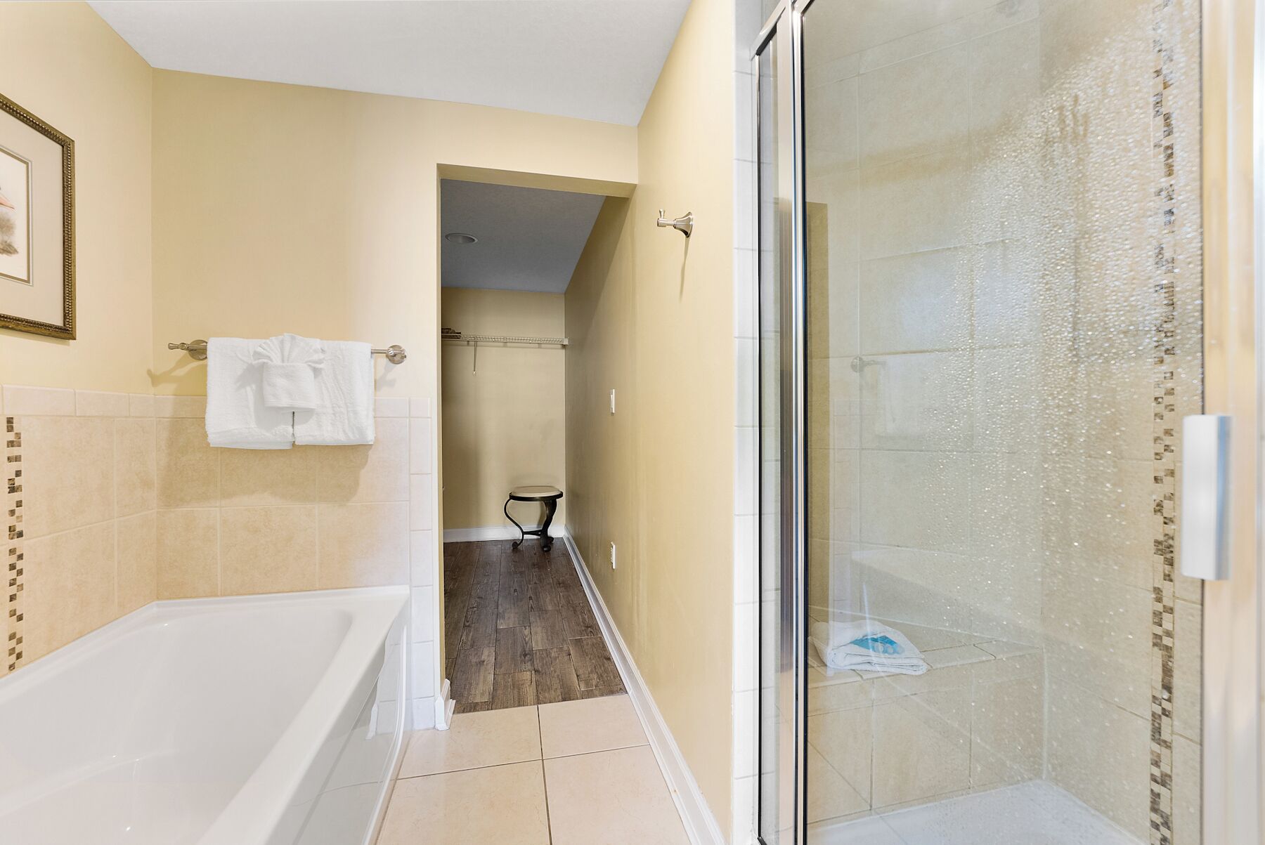 A bathroom with a bathtub, a shower with a glass door, and a small table with a towel.