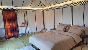 Una habitación con tienda, una cama, mesitas de noche y una cesta colgante.