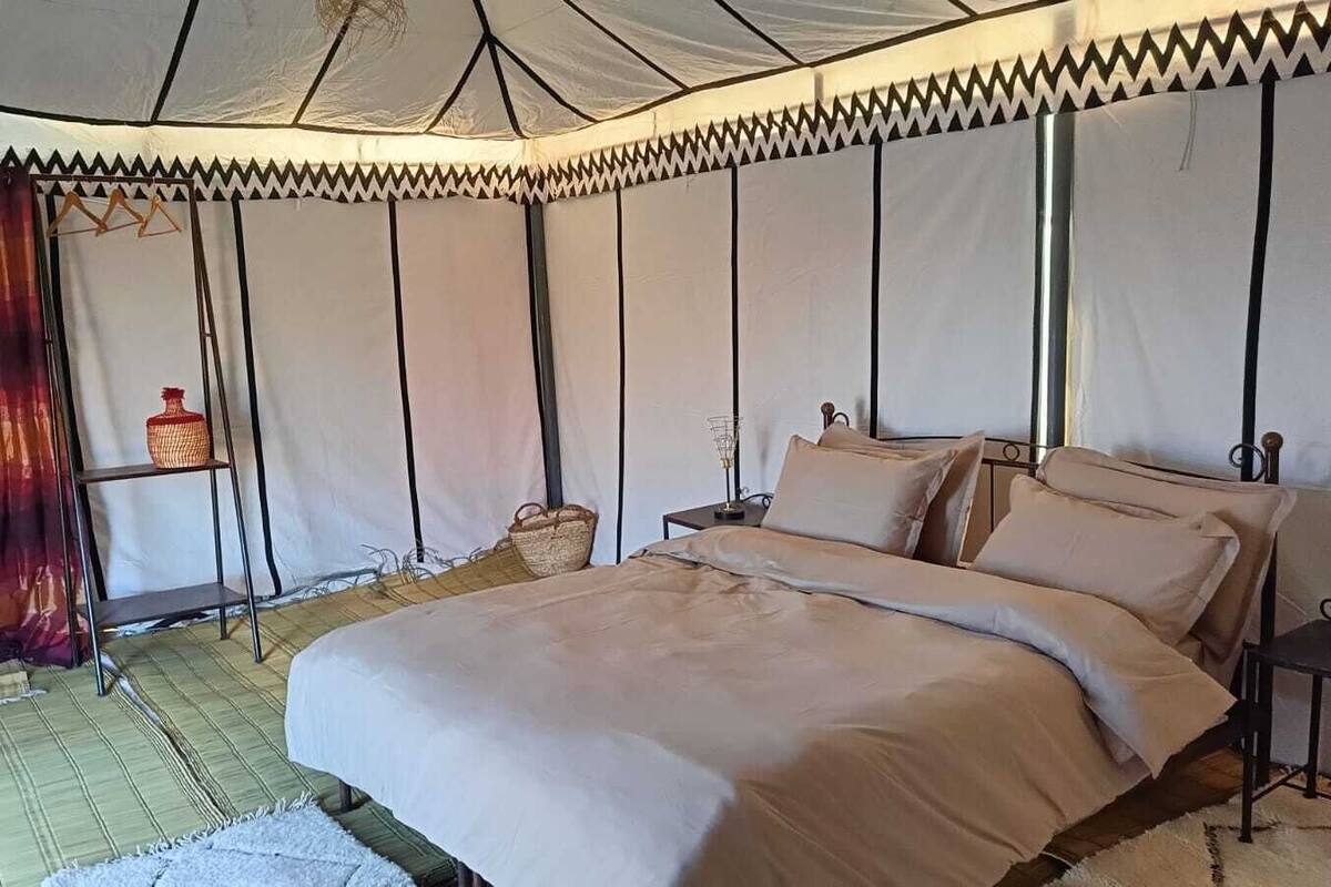 A tented room with a bed, bedside tables, and a hanging basket.