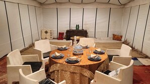 Una mesa de comedor redonda con mantel estampado, rodeada de sillas blancas con cojines negros.