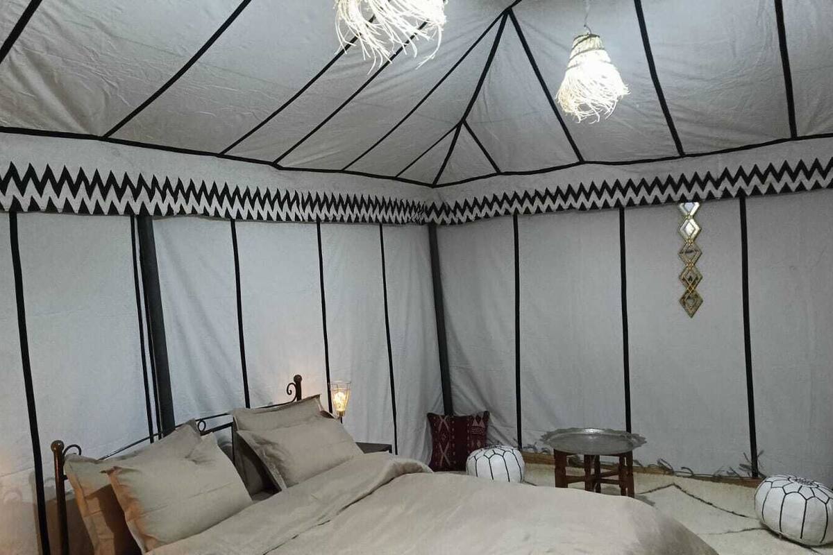 A tented room with a bed, bedside table, and hanging light fixtures.