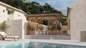 Et poolområde med et træbeklædt pergola, liggestole og en stenvæg.