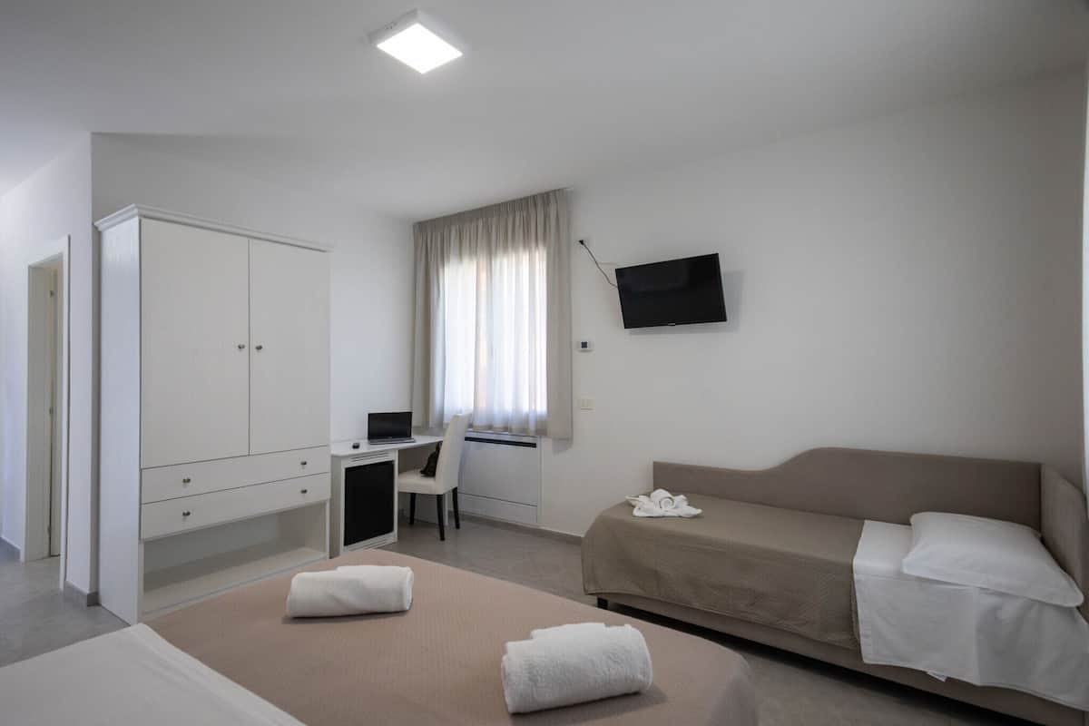 A hotel room with a bed, a desk with a laptop, a TV, and a wardrobe.