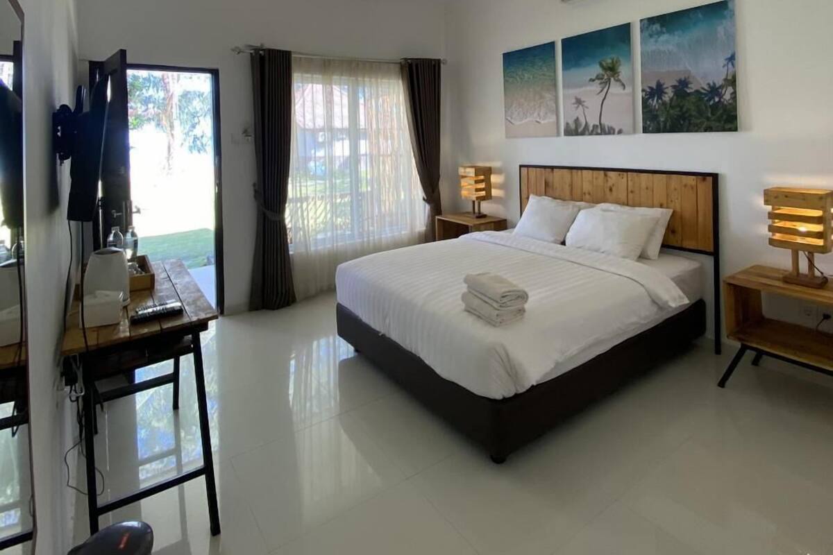 Quarto de hotel moderno com uma cama grande, luminárias de cabeceira, uma escrivaninha com um computador e vista para o exterior.