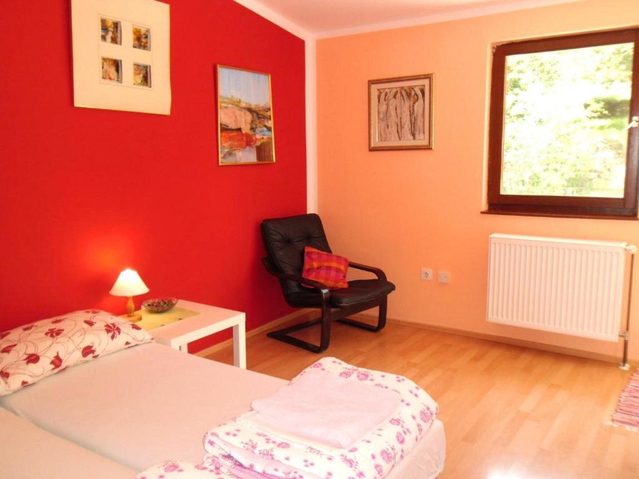 A bedroom with a bed, a chair, a lamp, and a window with a view of greenery.