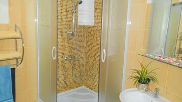 Une douche d’angle avec une porte en verre, un lavabo blanc et un miroir au-dessus du lavabo.
