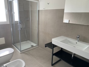 Ein modernes Badezimmer mit einer Duschkabine aus Glas, einem weißen Waschbecken und einer Toilette.