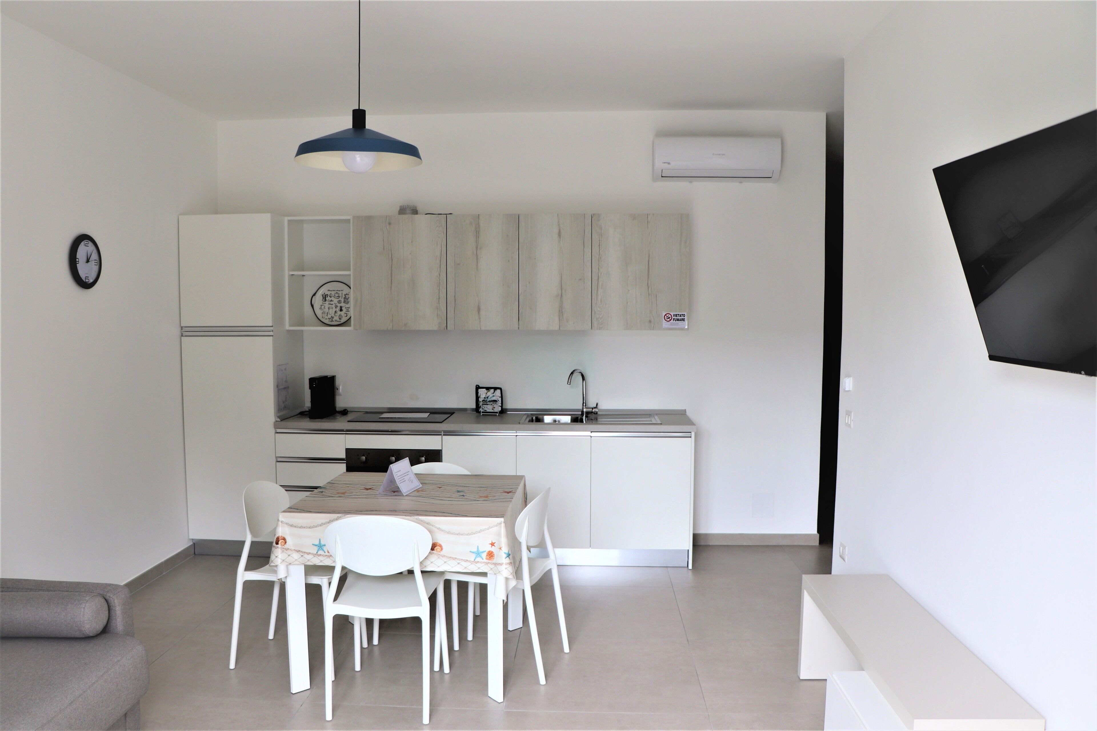 A modern kitchen with white cabinets, a dining table with chairs, and a blue pendant light.