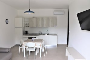 A modern kitchen with white cabinets, a dining table with chairs, and a blue pendant light. - Apartment in the center of Porto Cesareo, just a few steps from the sea (two-room apartment) (Porto Cesareo)