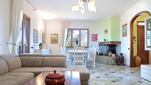 A living room with a sofa, a wooden table with a pot, a dining area with chairs and a table, and a fireplace. - Villa Velisia - Con Ampia Piscina E Campo Da Gioco Privato (Alessano)