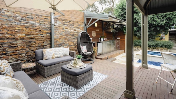 An outdoor patio with a stone wall, wicker furniture, a hanging chair, and a pool. - Luxury Retreat | Pool • Fireplace • Parking (Lower Plenty)