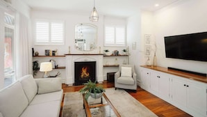 A living room with a fireplace, a sofa, a coffee table, and a television. - Luxury Retreat | Pool • Fireplace • Parking (Lower Plenty)