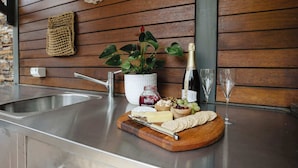 A kitchen counter with a wooden cutting board holding cheese, crackers, and a bottle of wine. - Luxury Retreat | Pool • Fireplace • Parking (Lower Plenty)