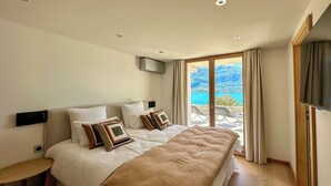 A modern bedroom with a large bed, a TV, and a balcony with a view. - APARTMENT with private terrace & lake view / 200 meters from lake & bike path (Sévrier)