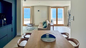 A modern living room with a wooden dining table, a sofa, and a view of the sea through large sliding doors. - APARTMENT with private terrace & lake view / 200 meters from lake & bike path (Sévrier)