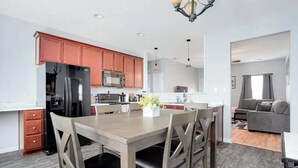 A modern kitchen with a dining area, featuring a refrigerator, stove, and cabinets.