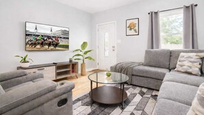 A modern living room with a grey sofa, a glass coffee table, and a mounted TV displaying a horse race.
