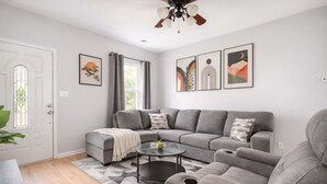 A modern living room with a grey sectional sofa, a glass coffee table, and a patterned rug.
