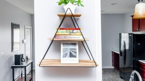 A kitchen with a black refrigerator, a wooden shelf with books and a plant, and a hanging light fixture.
