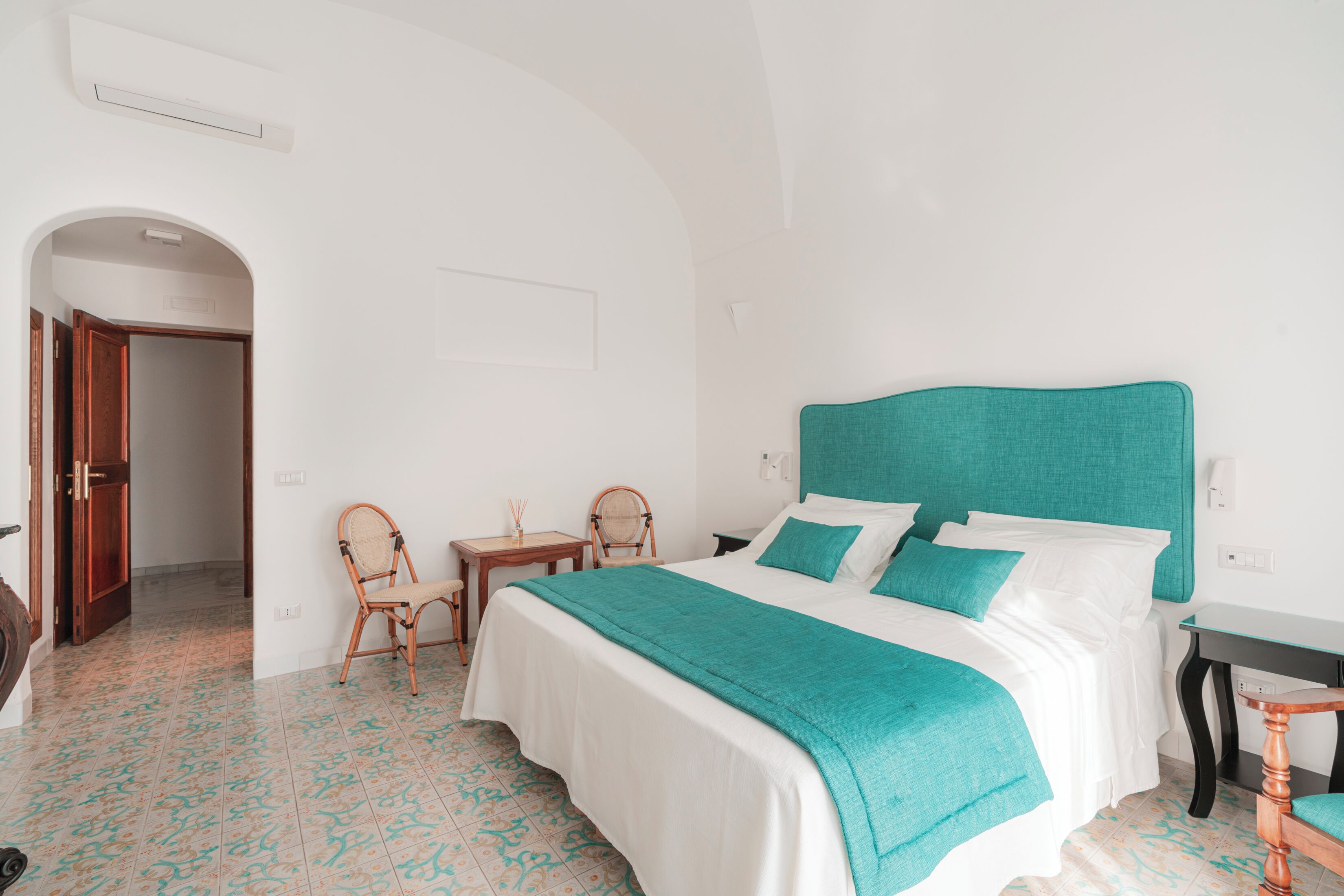 A bedroom with a bed, a chair, a small table, and an arched doorway.