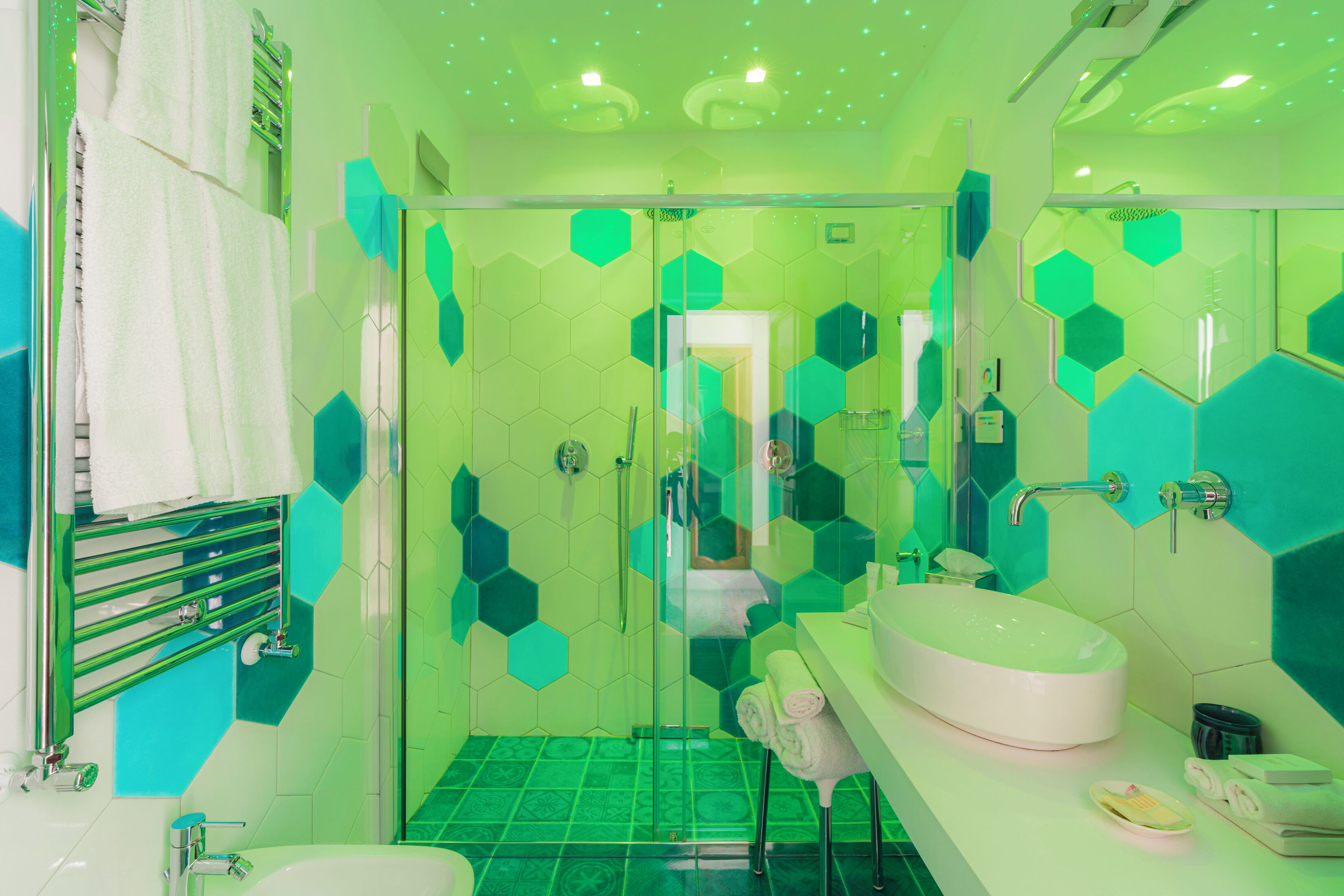 A bathroom with a glass shower enclosure, a white sink, and a green-tiled floor.