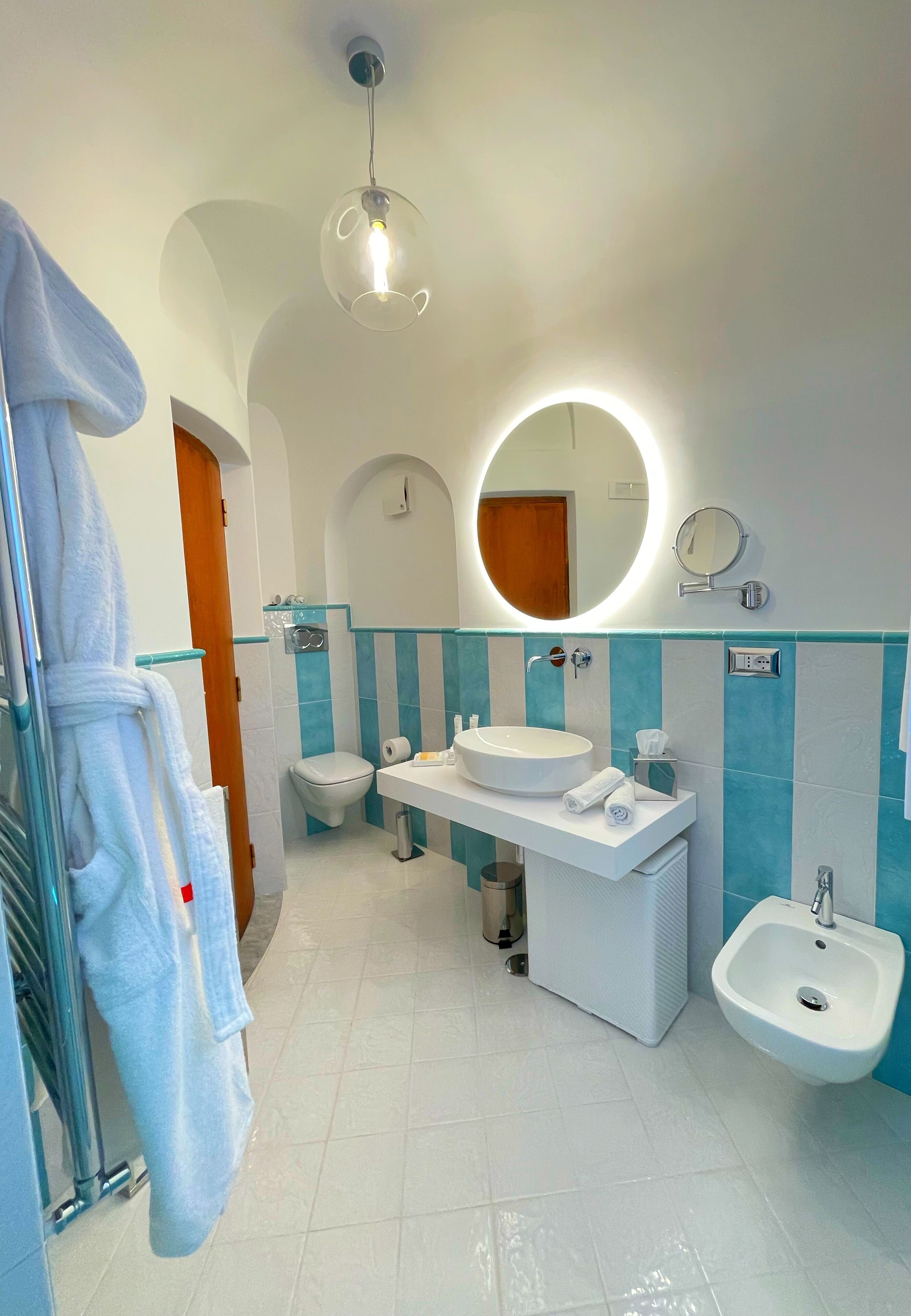 Un baño moderno con un espejo redondo, un lavabo, un bidé y un perchero para toallas.
