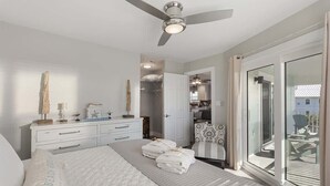 Une chambre à coucher avec un lit, un ventilateur de plafond, une commode et une vue sur l’extérieur.