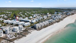 Une vue aérienne d’une station balnéaire avec de nombreux bâtiments, une plage de sable et un ciel bleu dégagé.