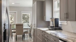 A modern kitchen with grey cabinets, a marble countertop, and a dining area with a glass table and chairs. - Lake escape w/ kayaks, bikes & 5-min beach (Santa Rosa Beach)