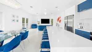 A modern kitchen with a large refrigerator, a coffee maker, and a dining area with blue chairs and a glass table. - Azul Paradise ~ Waterfront ~ Games ~ Pool ~ Dock (Marathon)