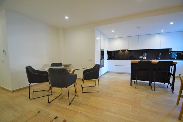 A modern kitchen with white cabinets, a wooden countertop, and black chairs. - Baia Mar in S o Martinho do Porto (Alcobaça)
