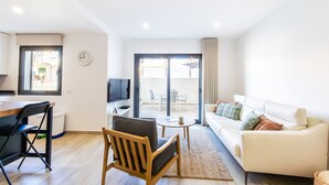 Un salon moderne avec un canapé, une table à manger, un téléviseur et un balcon équipé de chaises.