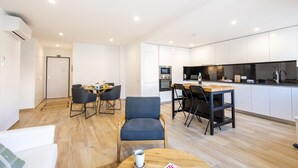 Une cuisine moderne avec des meubles blancs, un coin repas avec une table et des chaises, et un salon avec un canapé et une table basse.