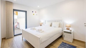 Une chambre d’hôtel moderne avec un grand lit, deux tables de chevet avec des lampes, un tapis bleu et une porte coulissante donnant sur un balcon.
