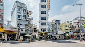 A multi-story hotel with a prominent sign, several ground-level shops, and a busy street scene. -  Cozrum - Love Hotel Trần Thị Nghỉ (Ho Chi Minh City)