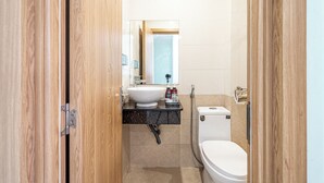 A compact bathroom with a wooden door, a white sink, a small toilet, and a mirror above the sink. -  Cozrum - Love Hotel Trần Thị Nghỉ (Ho Chi Minh City)
