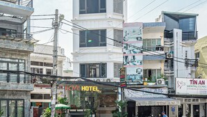A multi-story hotel with a prominent sign, a dental clinic across the street, and several motorcycles parked outside. -  Cozrum - Love Hotel Trần Thị Nghỉ (Ho Chi Minh City)